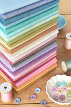 A stack of folded Tilda chambray fabrics with Tilda chambray covered buttons